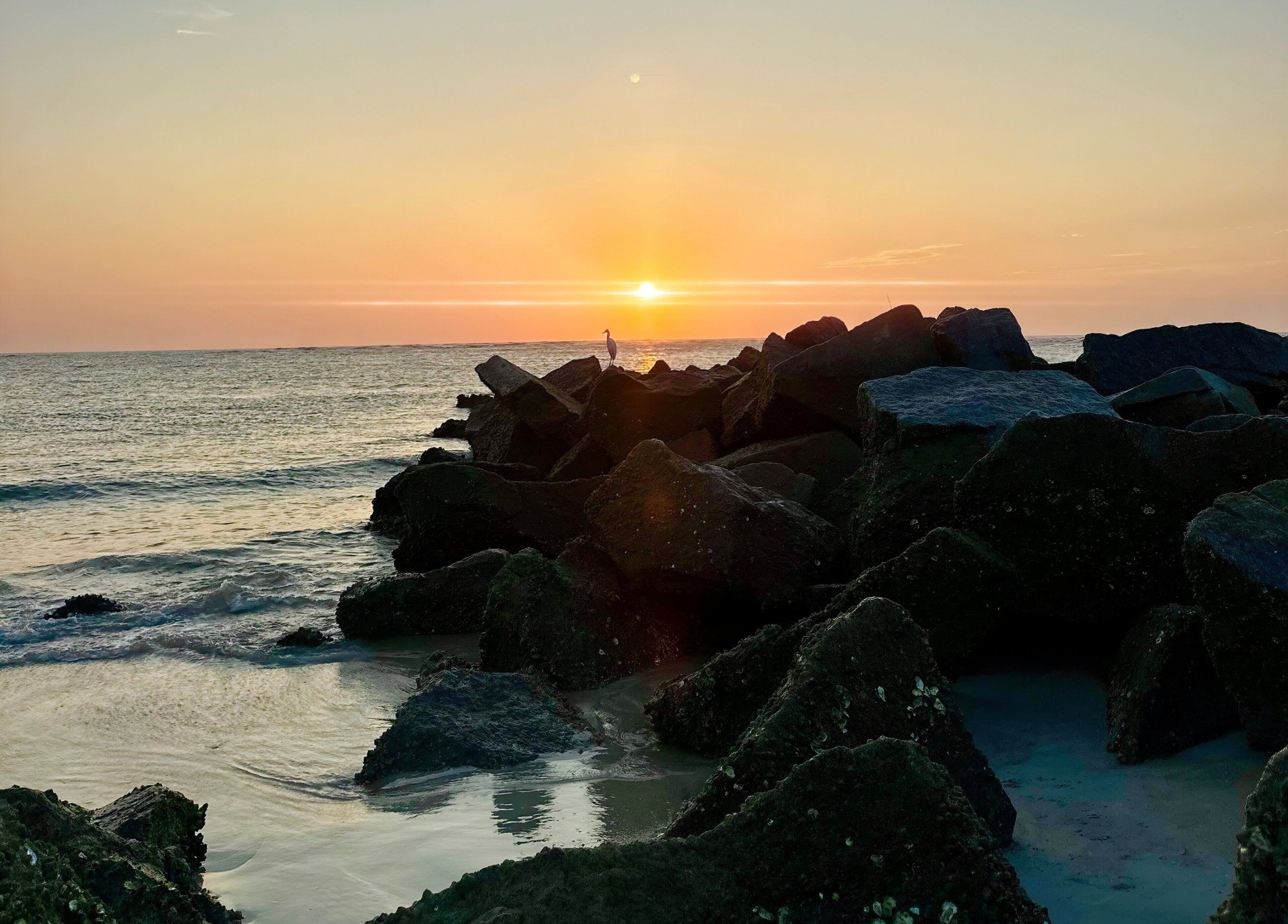 A sunset over a rocky coastline with waves crashing against the rocks.