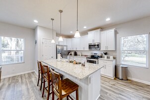 Una cocina moderna con armarios blancos, una isla de granito e iluminación colgante.