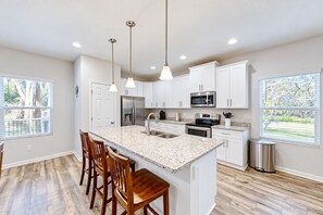 A kitchen with white cabinets, a granite countertop, stainless steel appliances, and wooden chairs. - Newly-built 2-story Home Near the Ocean With Patio, Washer/dryer, Streaming (Jacksonville)