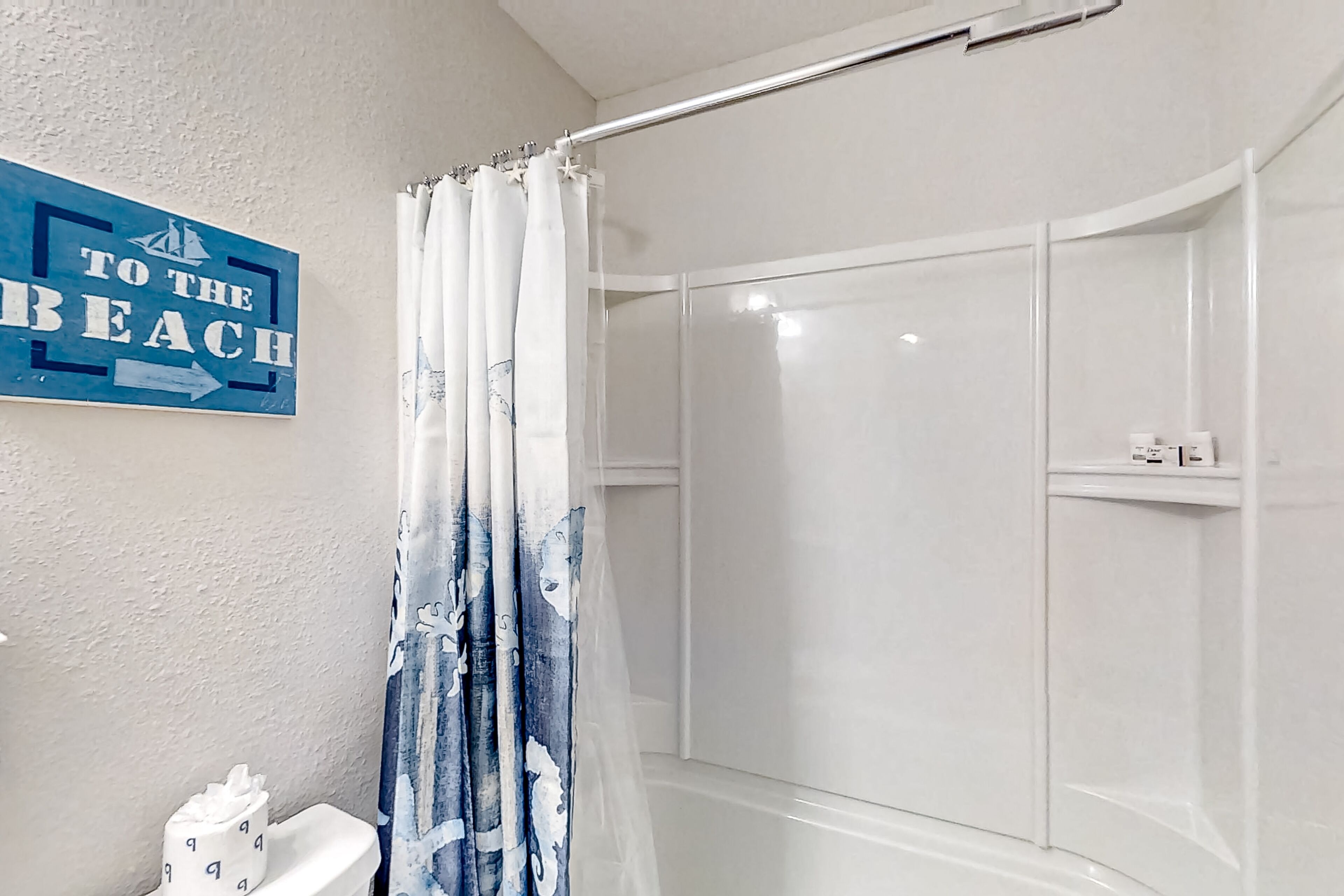 Et badeværelse med bruser, toilet og et skilt, der står "TO THE BEACH".