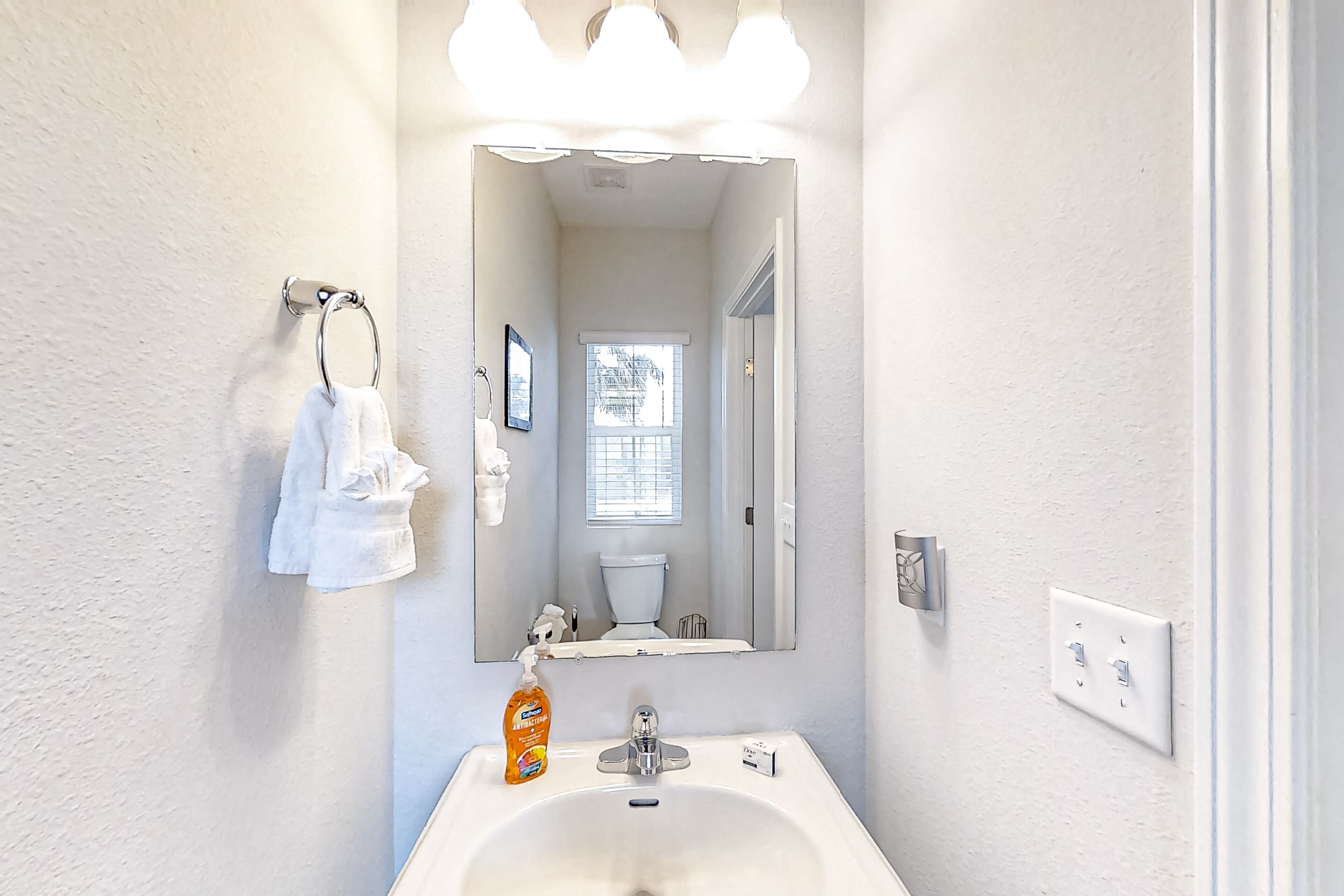 Un baño con lavamanos blanco, un espejo y un perchero para toallas.