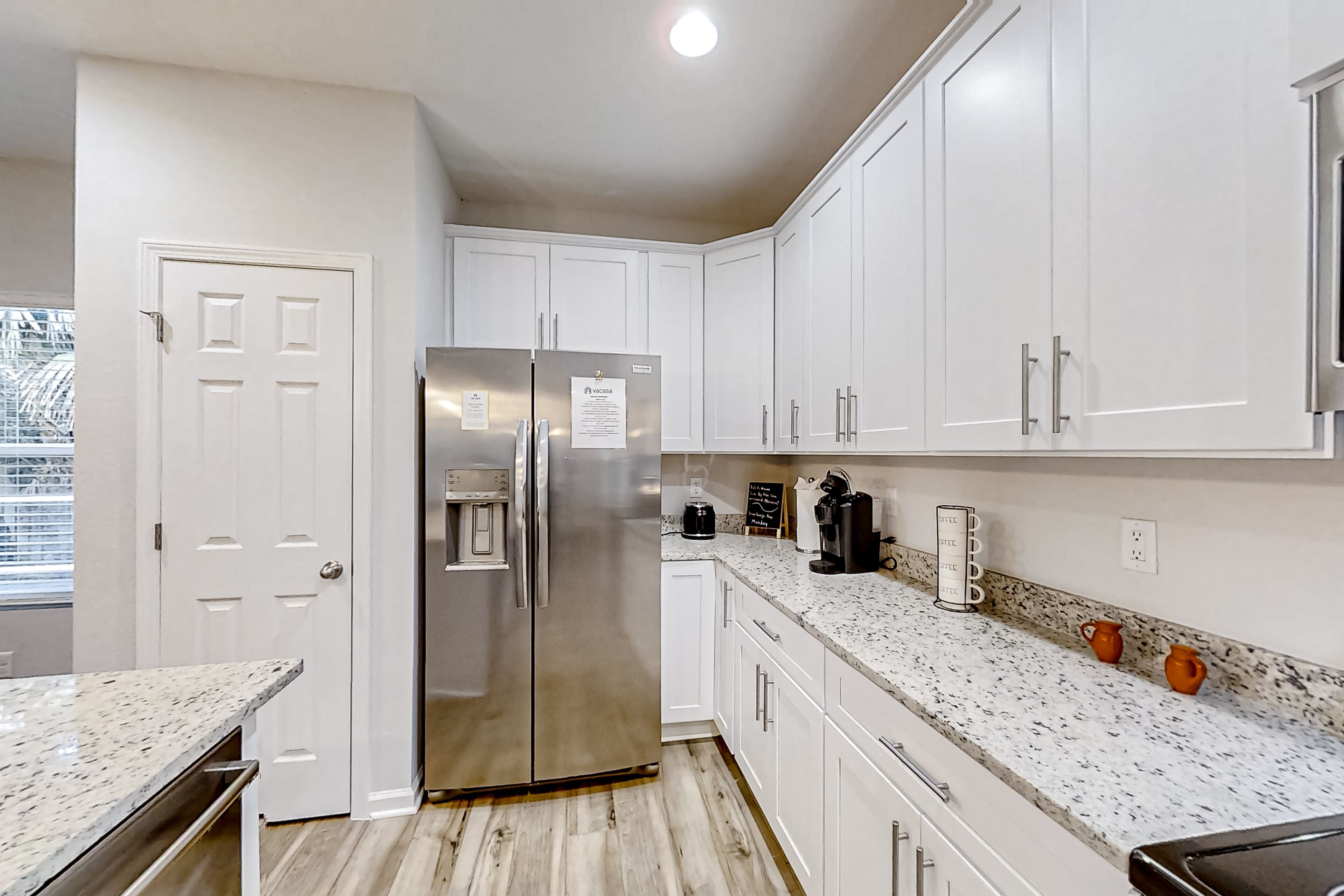 A modern kitchen with white cabinetry, a stainless steel refrigerator, a coffee maker, and a coffee mug on the counter.