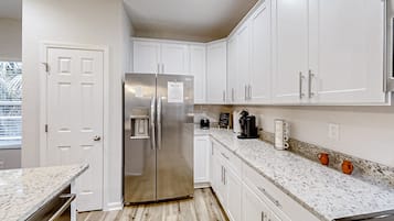 A modern kitchen with white cabinetry, a stainless steel refrigerator, a coffee maker, and a coffee mug on the counter.