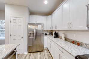 A modern kitchen with white cabinetry, a stainless steel refrigerator, a coffee maker, and a coffee mug on the counter. - Newly-built 2-story Home Near the Ocean With Patio, Washer/dryer, Streaming (Jacksonville)