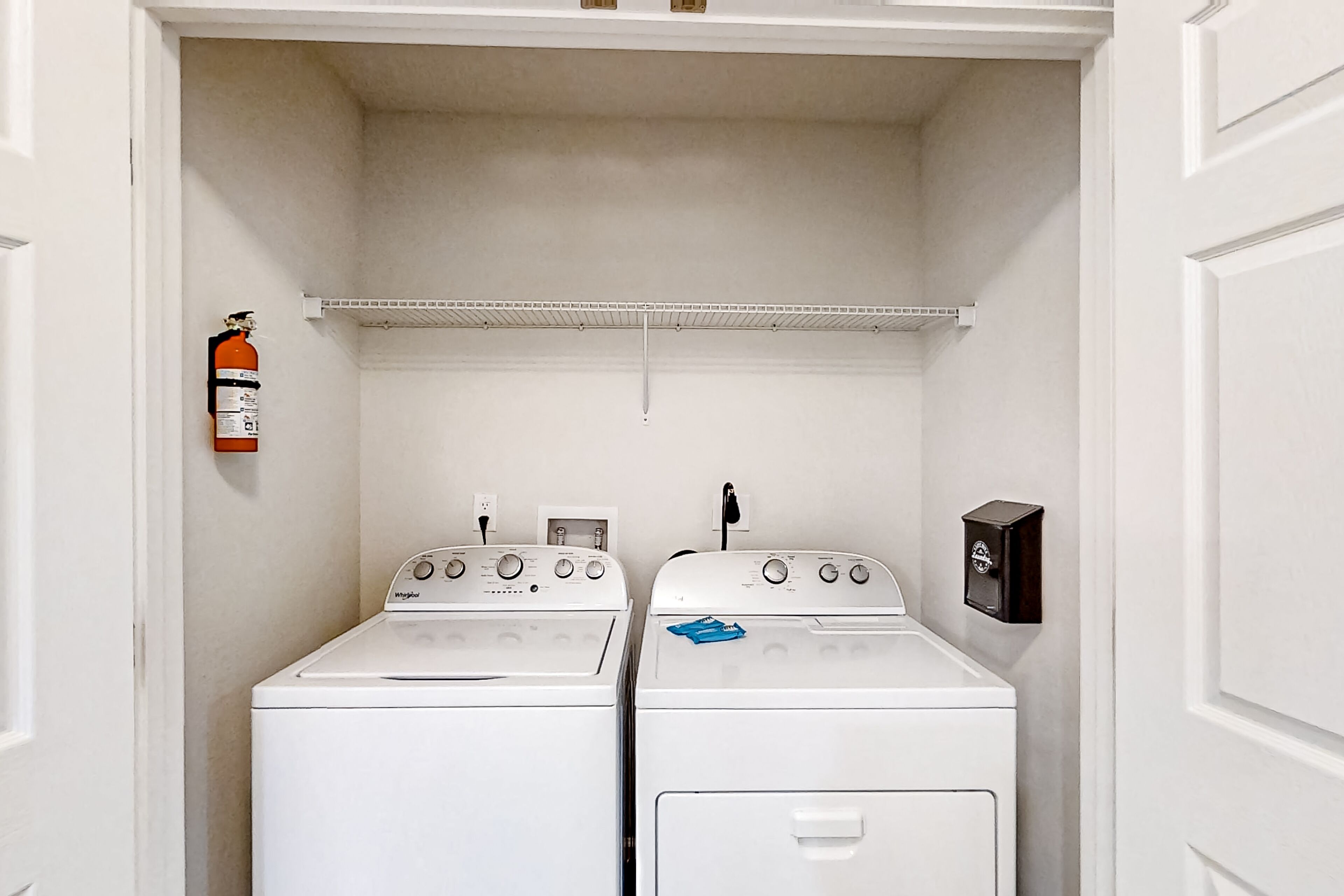 A laundry room with two white washers and dryers, a fire extinguisher, and a utility box on the wall.