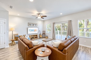 A spacious living room with a brown leather sofa, a wooden coffee table, and a ceiling fan. - Newly-built 2-story Home Near the Ocean With Patio, Washer/dryer, Streaming (Jacksonville)