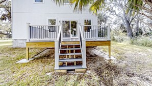 Une maison blanche avec une terrasse en bois et un escalier menant à un balcon.