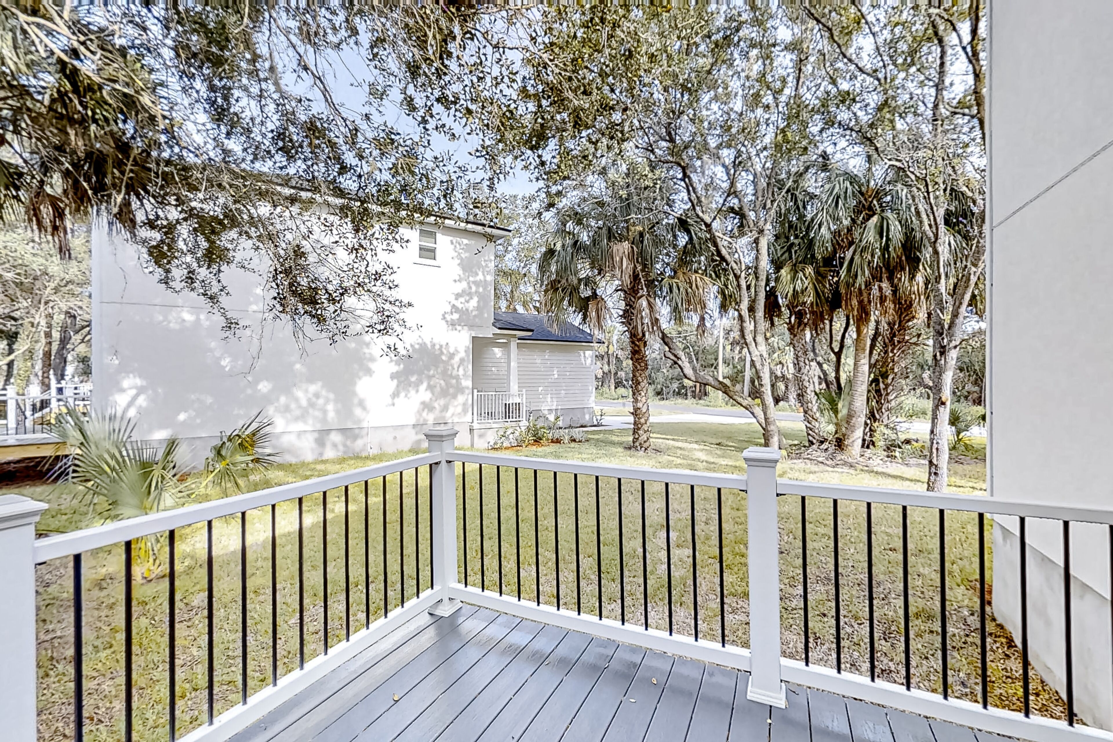 A wooden deck with a white railing, a white building in the background, and surrounding trees.