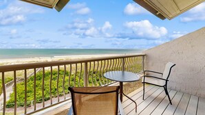 Een balkon met uitzicht op het strand, een tafel en twee stoelen.