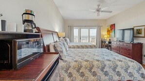 Een hotelkamer met een bed, een bureau met koffiezetapparaat, een televisie en een balkon met gordijnen.