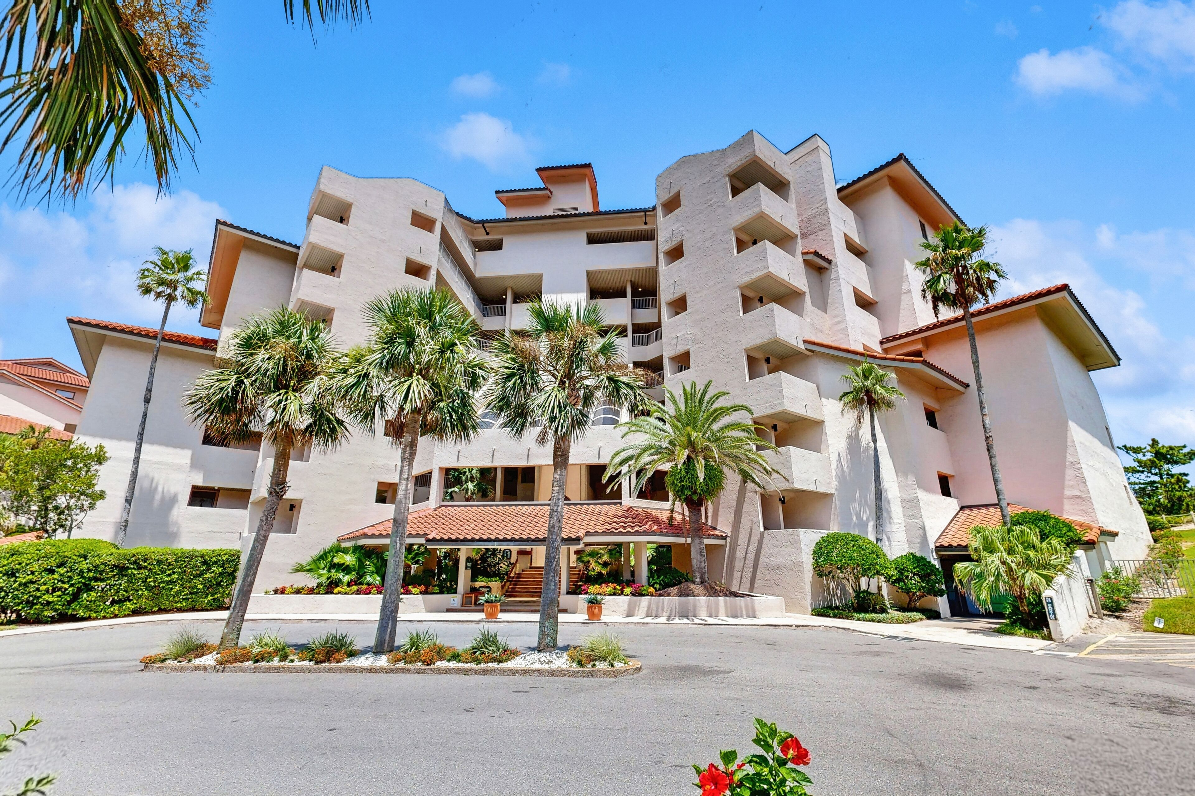 A multi-story hotel with a central courtyard, palm trees, and a red-tiled roof.