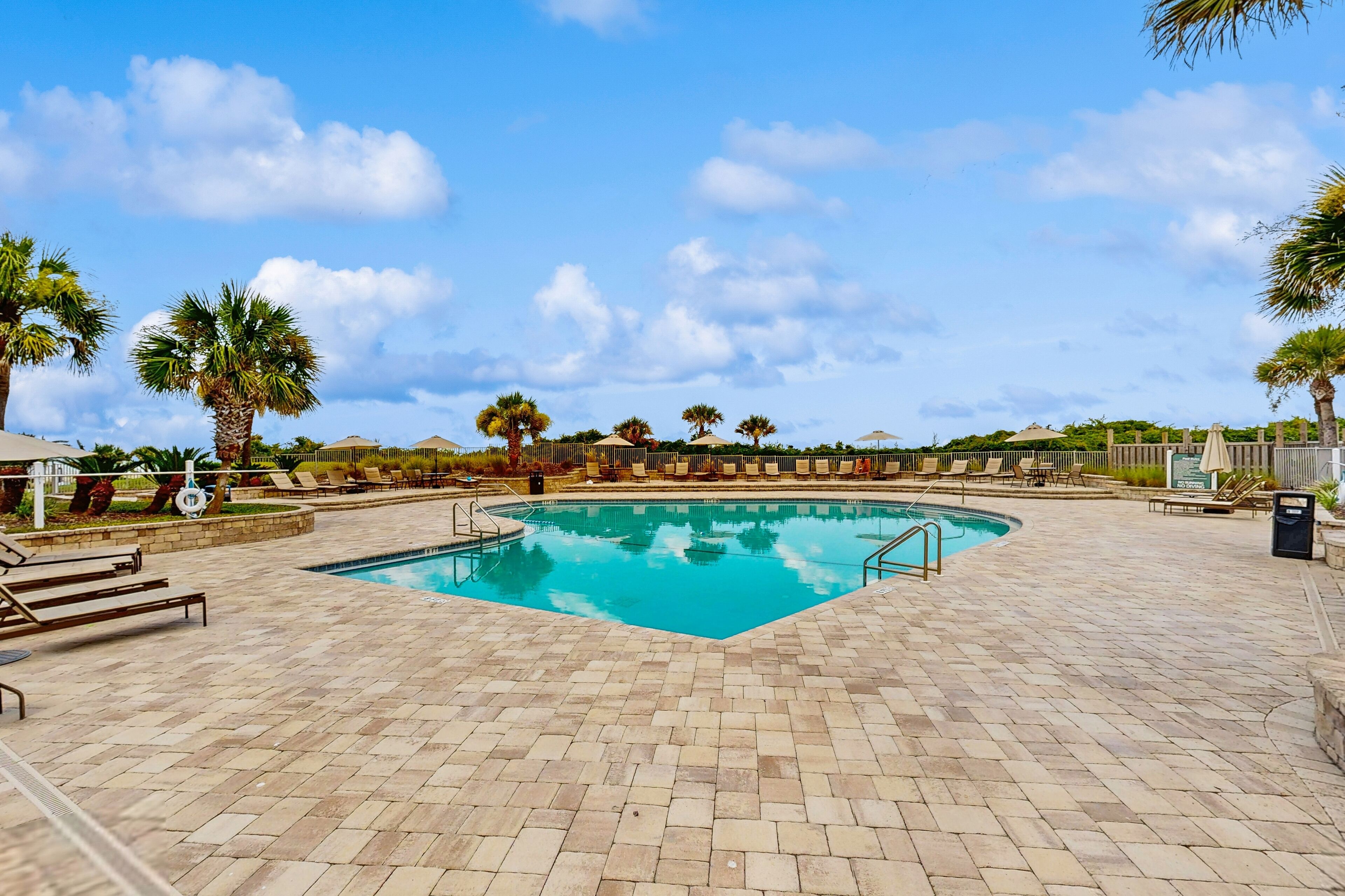 A swimming pool with a tiled deck, surrounded by palm trees and lounge chairs.