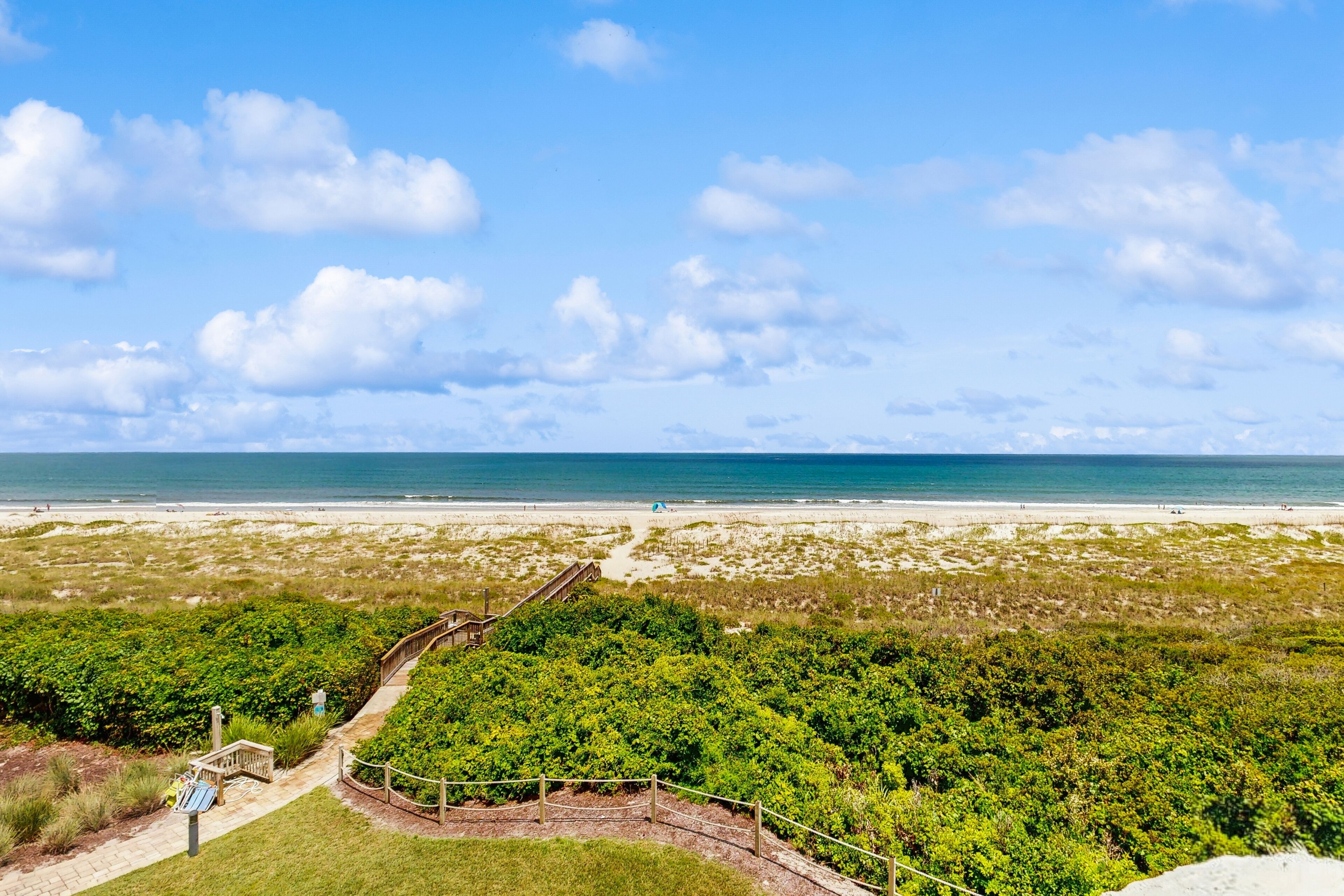 Vista de playa con un sendero que conduce a la orilla, rodeado de vegetación.