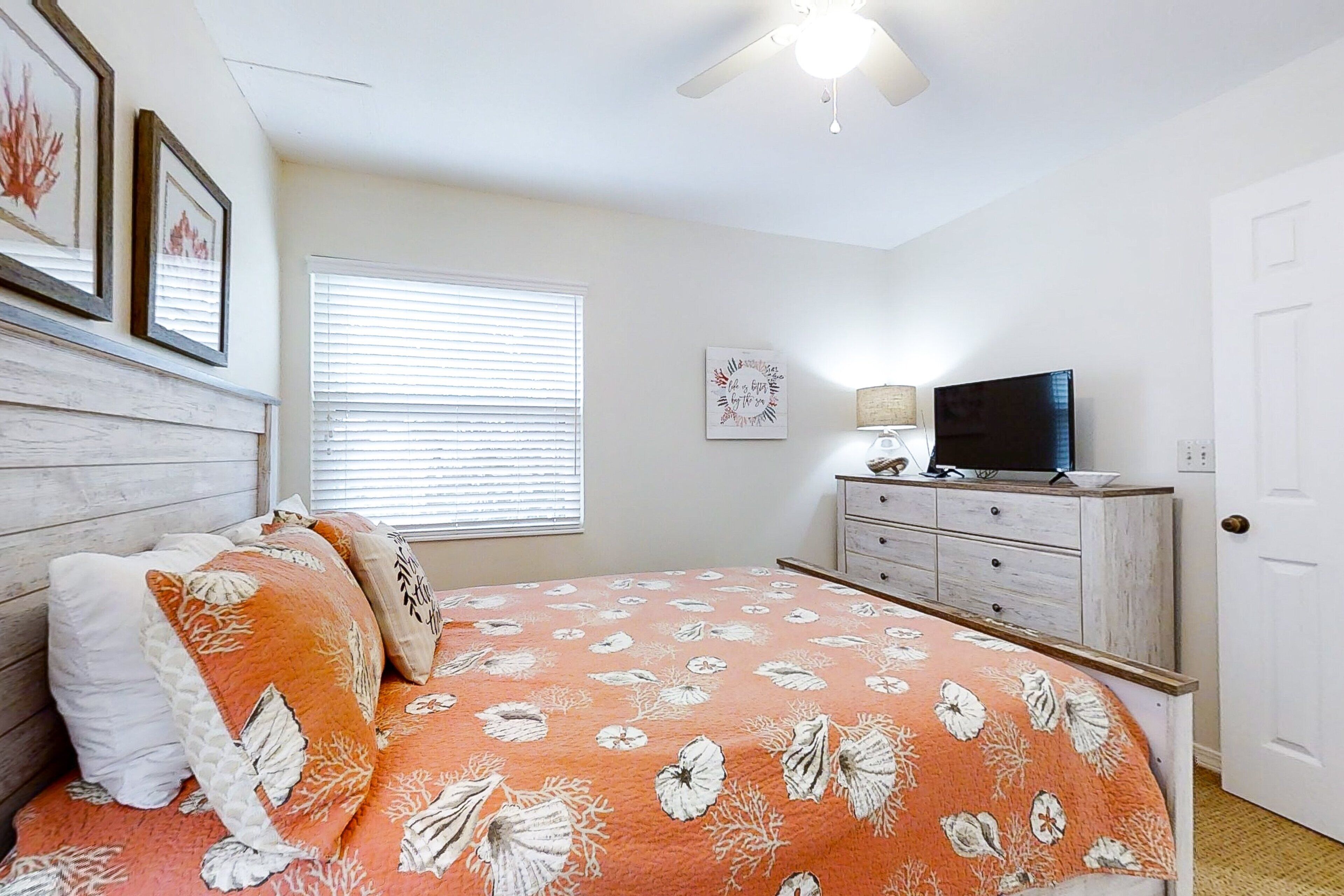 A bedroom with a bed, a dresser, a television, and a ceiling fan.