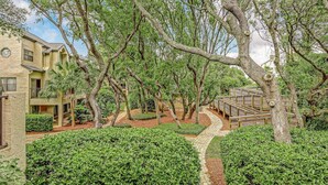 Une cour avec un chemin pavé, entourée de haies et d’arbres bien entretenus.