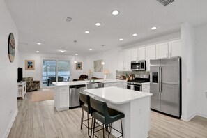 A modern kitchen with white cabinetry, stainless steel appliances, and a central island with bar stools. - New Dog-friendly Home Near Vilano Beach With Private hot Tub, Grill, W/d, & AC (St. Augustine)