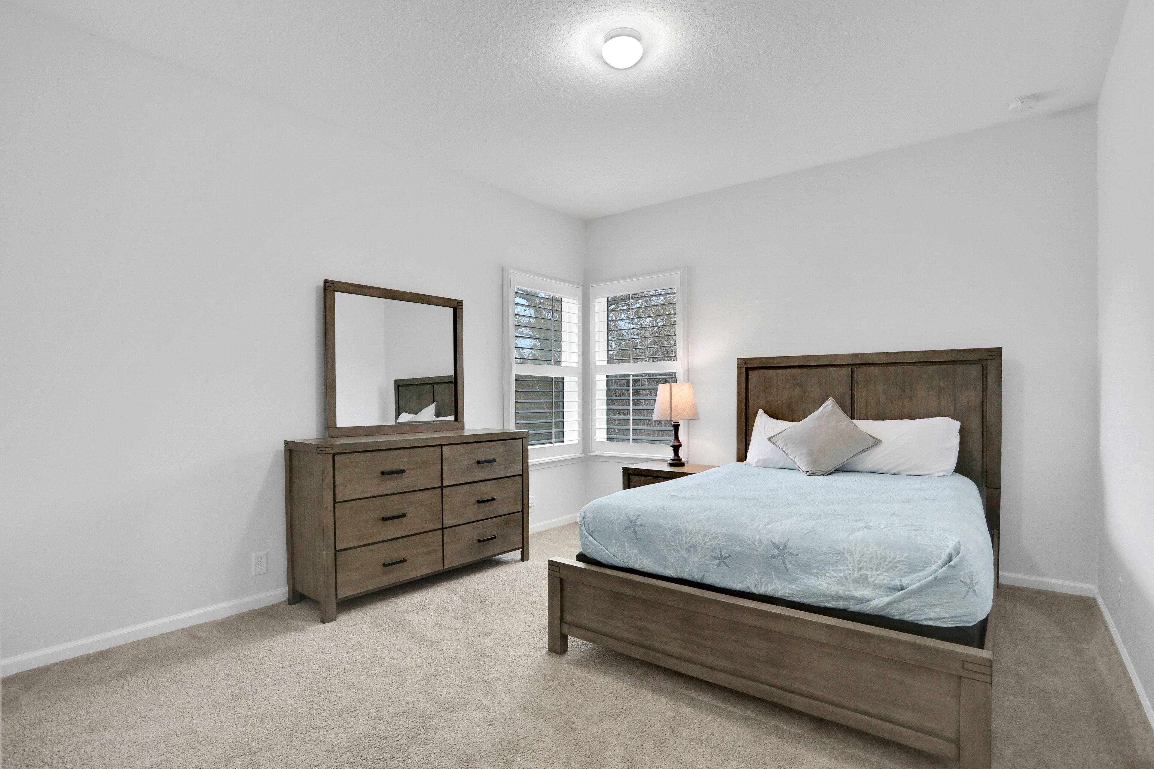 A bedroom with a wooden bed, a dresser, a mirror, and a window with blinds.