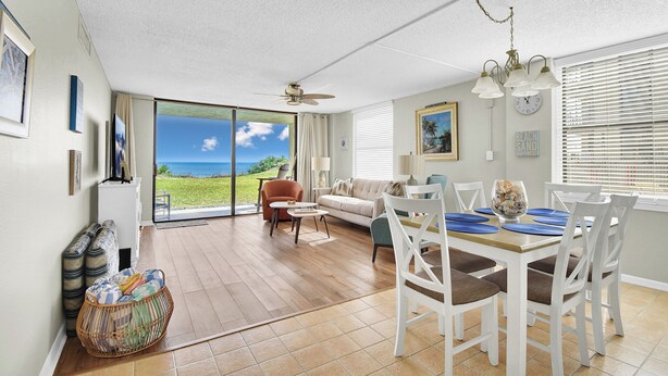 A spacious living area with a large sliding glass door leading to a balcony, a dining table with chairs, a sofa, and a ceiling fan. - Newly Decorated Ground-floor Suite Steps From Beach and Pool W/views, Wifi (St. Augustine)