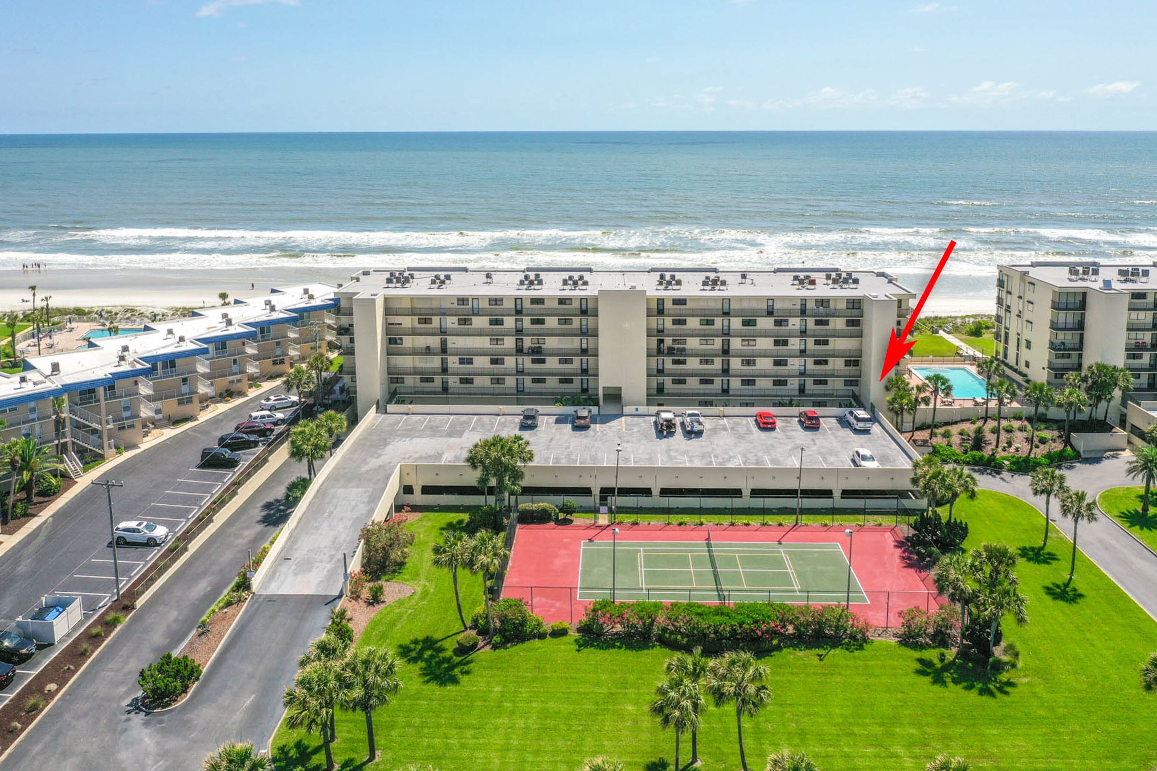 Un hotel con diversi piani, un parcheggio, un campo da tennis e vista sulla spiaggia.