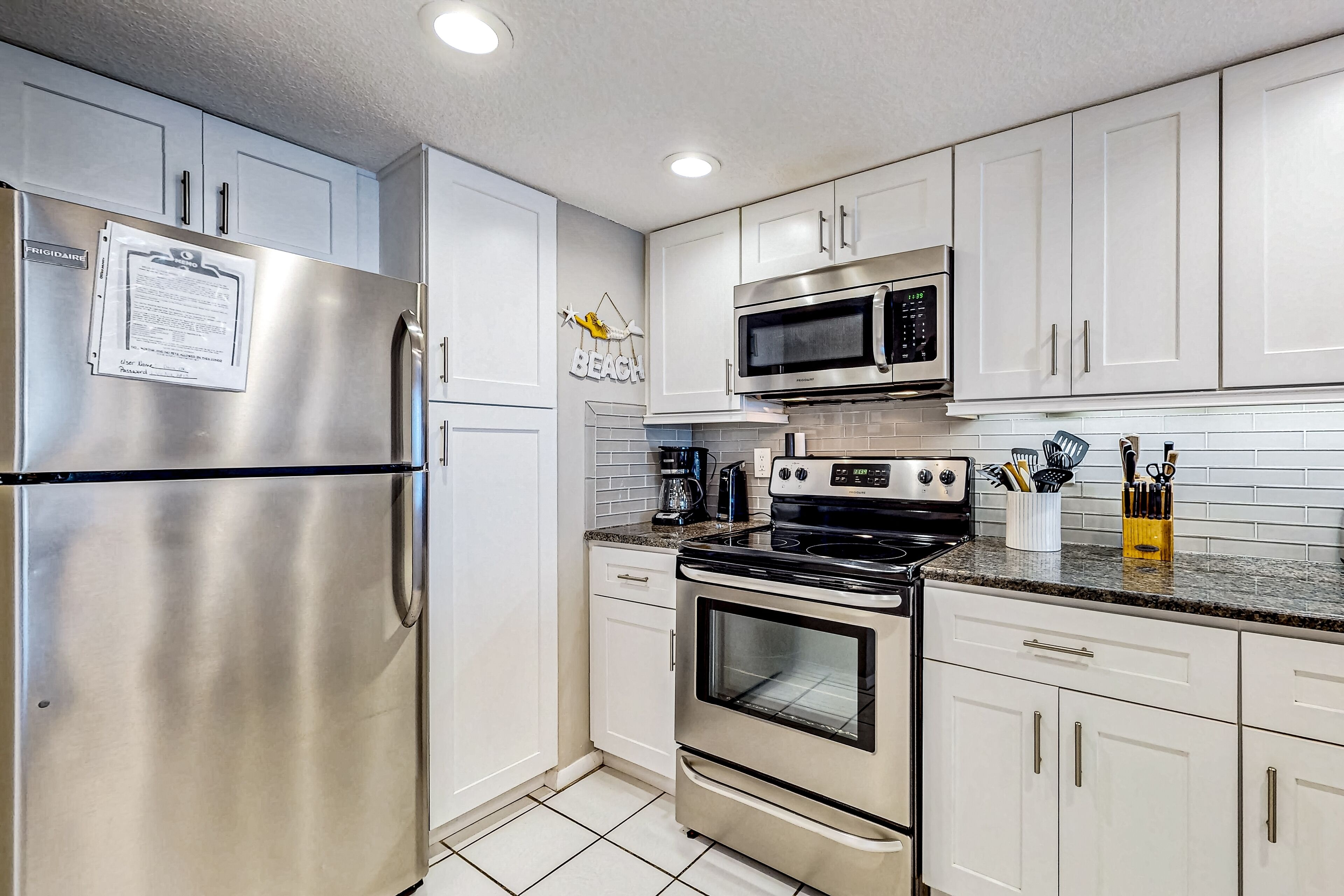 A modern kitchen with stainless steel appliances, white cabinets, and a tiled backsplash.