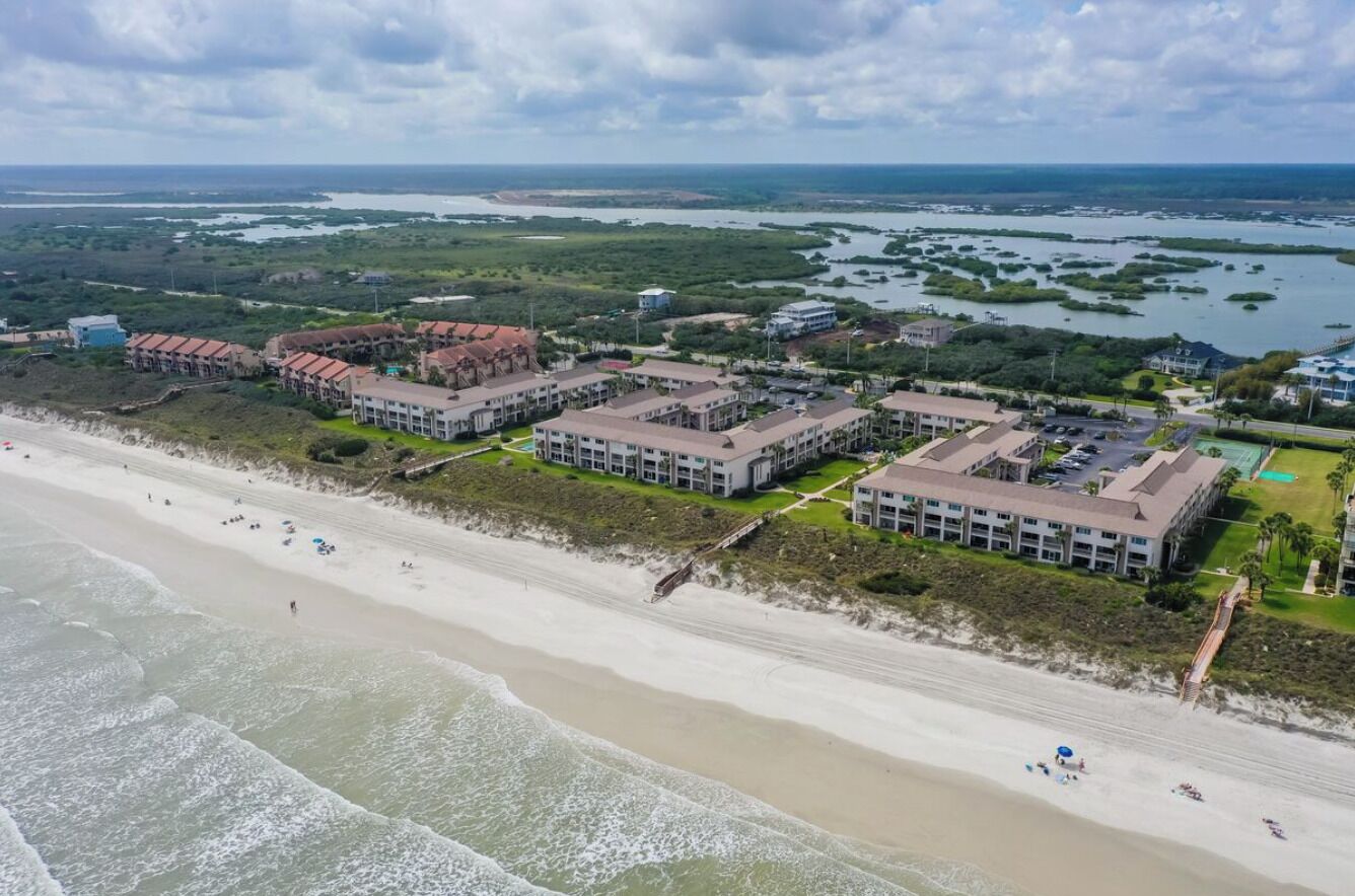 Luftaufnahme eines Küstenhotels mit mehreren Gebäuden, einem Strand und einem Yachthafen.