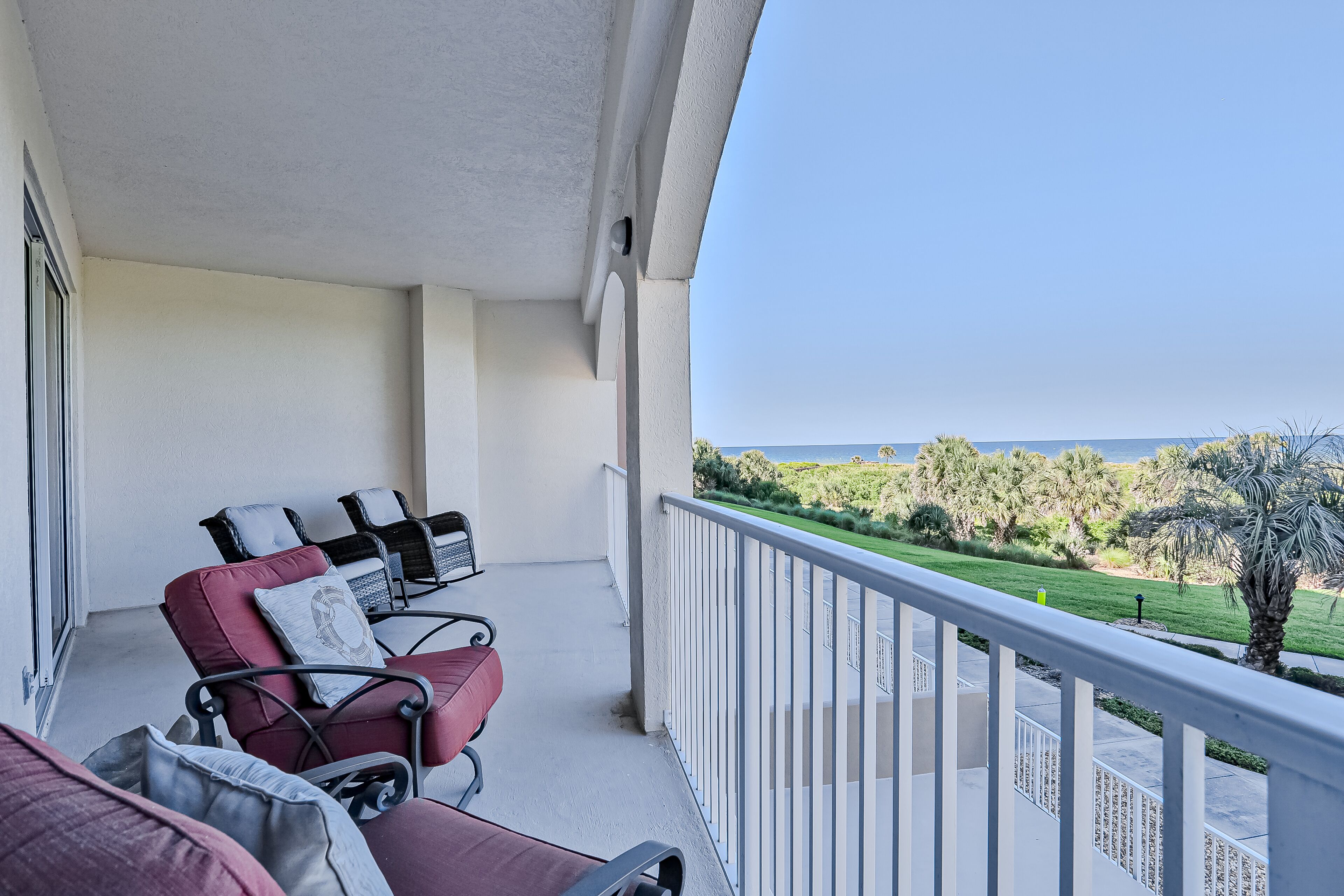 Un balcone con due sedie rosse e un tavolo, con vista su un paesaggio verde e il mare.