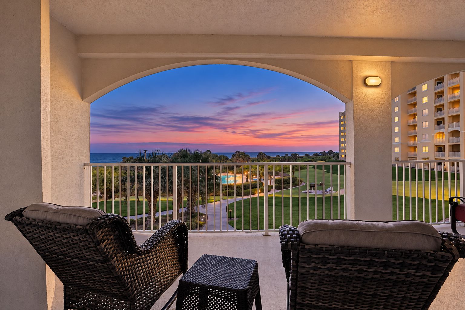 A balcony with wicker furniture overlooking a golf course and a building with balconies.