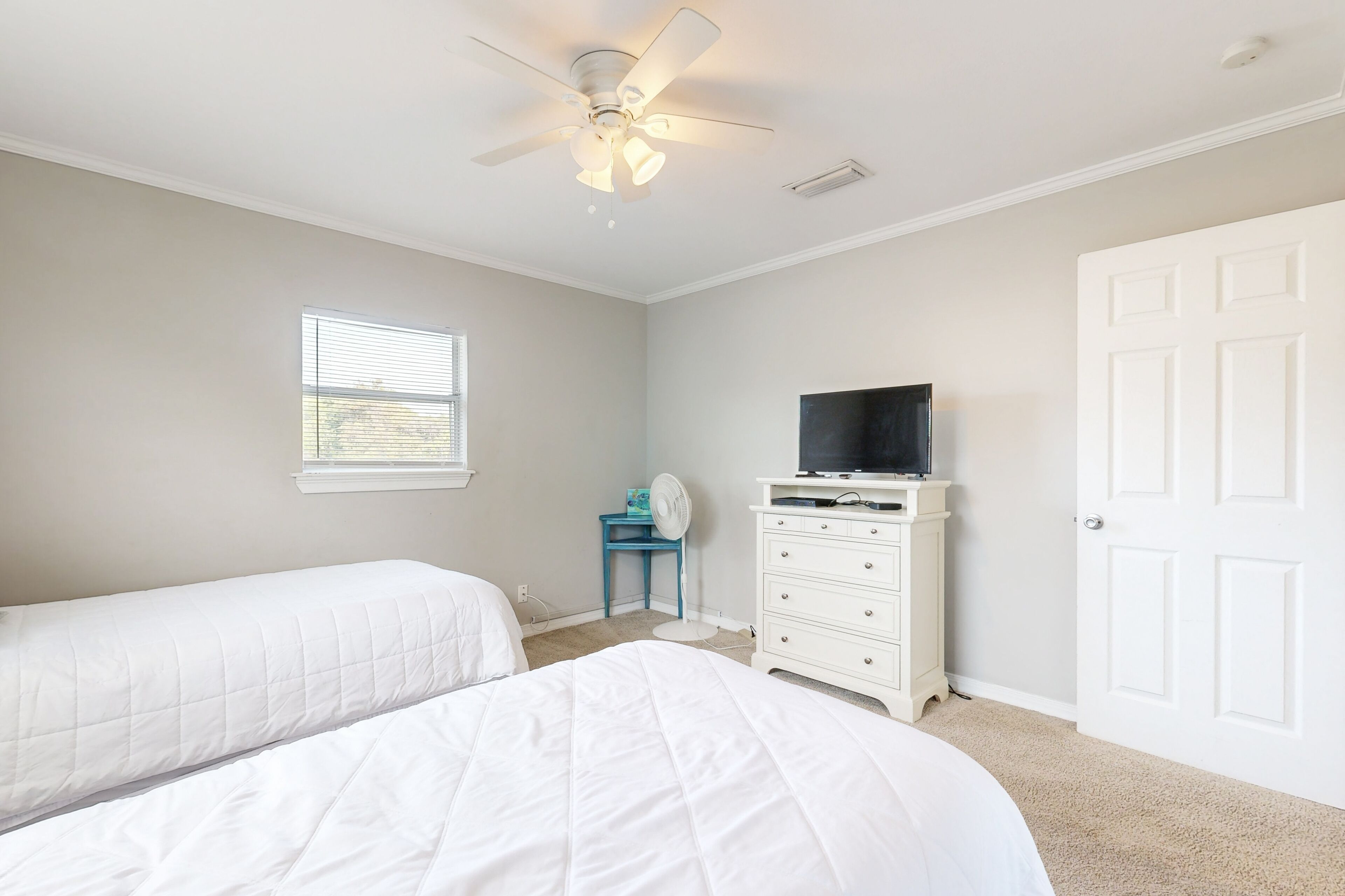 A bedroom with two beds, a ceiling fan, a dresser, a television, and a window.