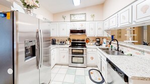 A modern kitchen with stainless steel appliances, white cabinetry, and decorative elements like palm trees and seashells on the walls. - Jacksonville's Delight House in Jacksonville With Pool on St Johns River (Jacksonville)