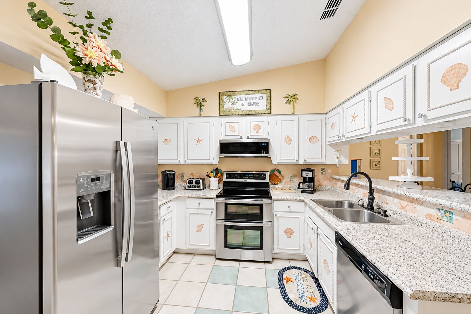A modern kitchen with stainless steel appliances, white cabinetry, and decorative shell motifs.