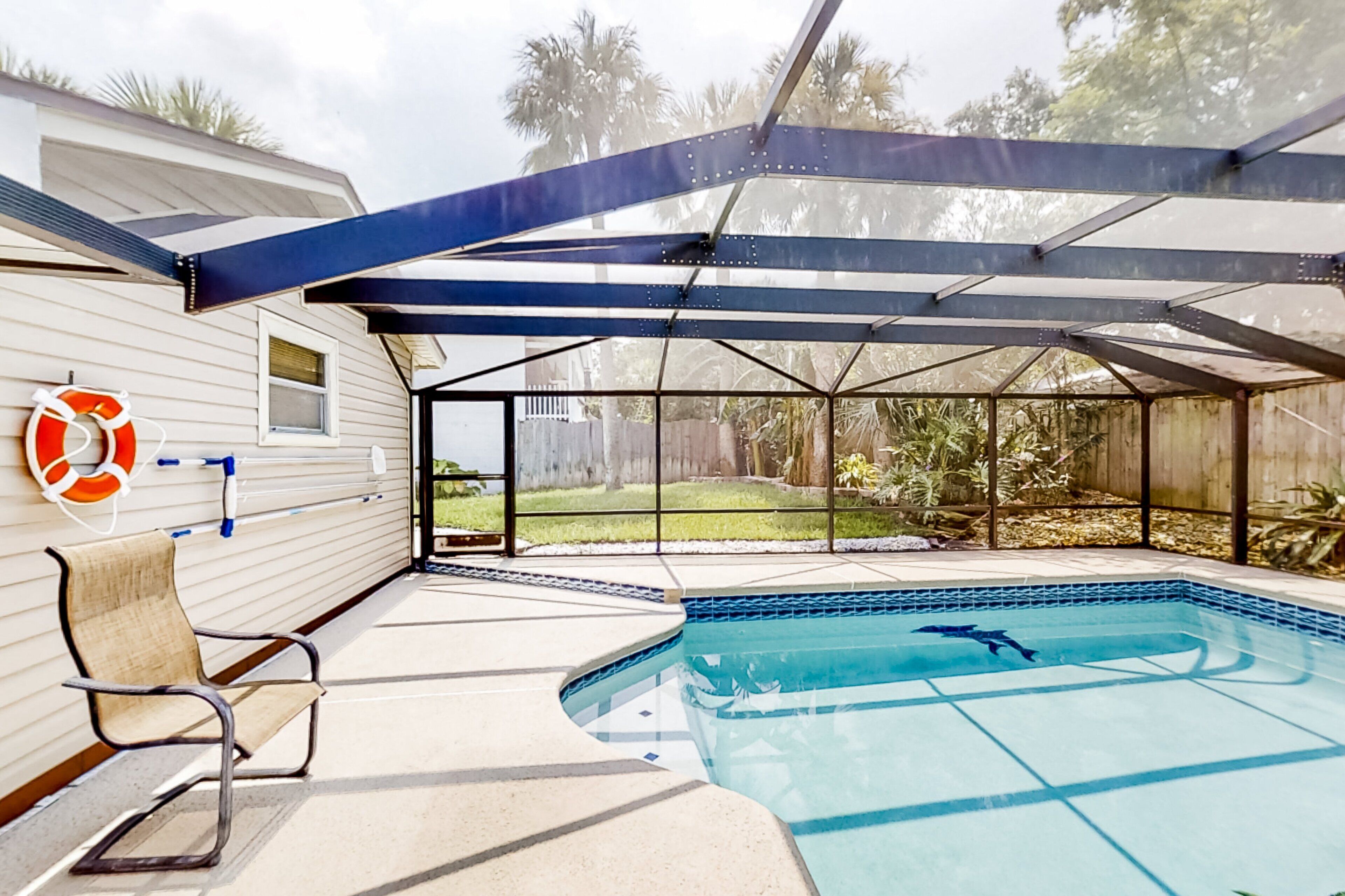 A covered outdoor swimming pool with a lifebuoy, a bench, and a view of a backyard.