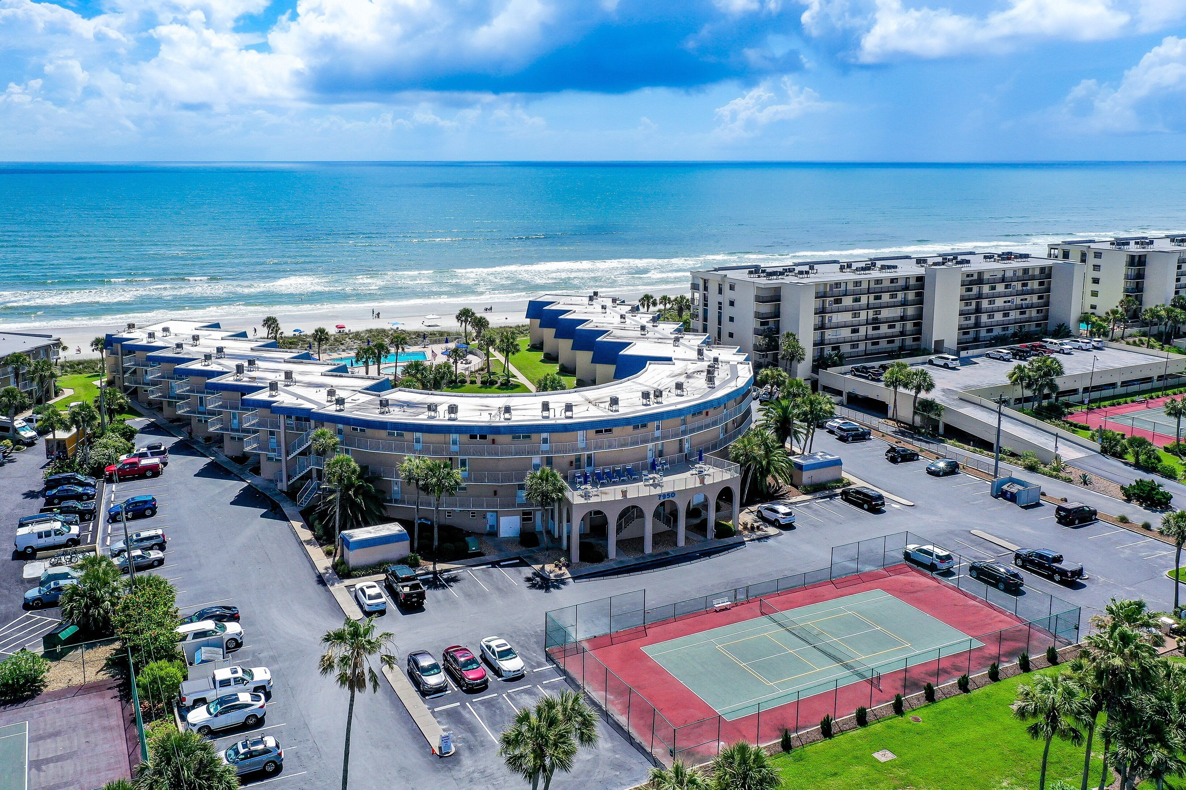 Een hotel met een zwembad op het dak, een tennisbaan en uitzicht op de oceaan.