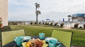 Una mesa con desayuno, que incluye frutas y pasteles, con vista a una playa con palmeras y una valla.