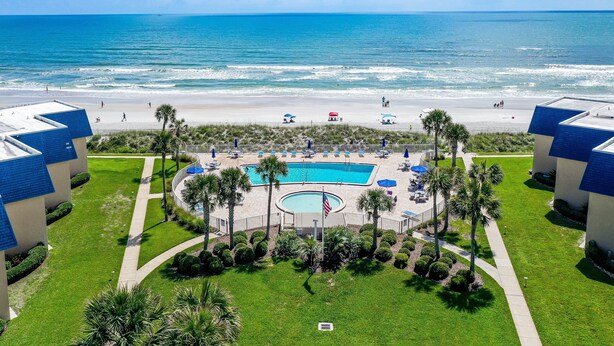Un resort con piscina, acceso a la playa y palmeras.