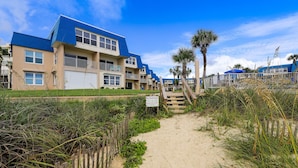 Un hotel frente a la playa con un camino de arena que lleva a la entrada, rodeado de palmeras y un letrero de 'No Entrar'.