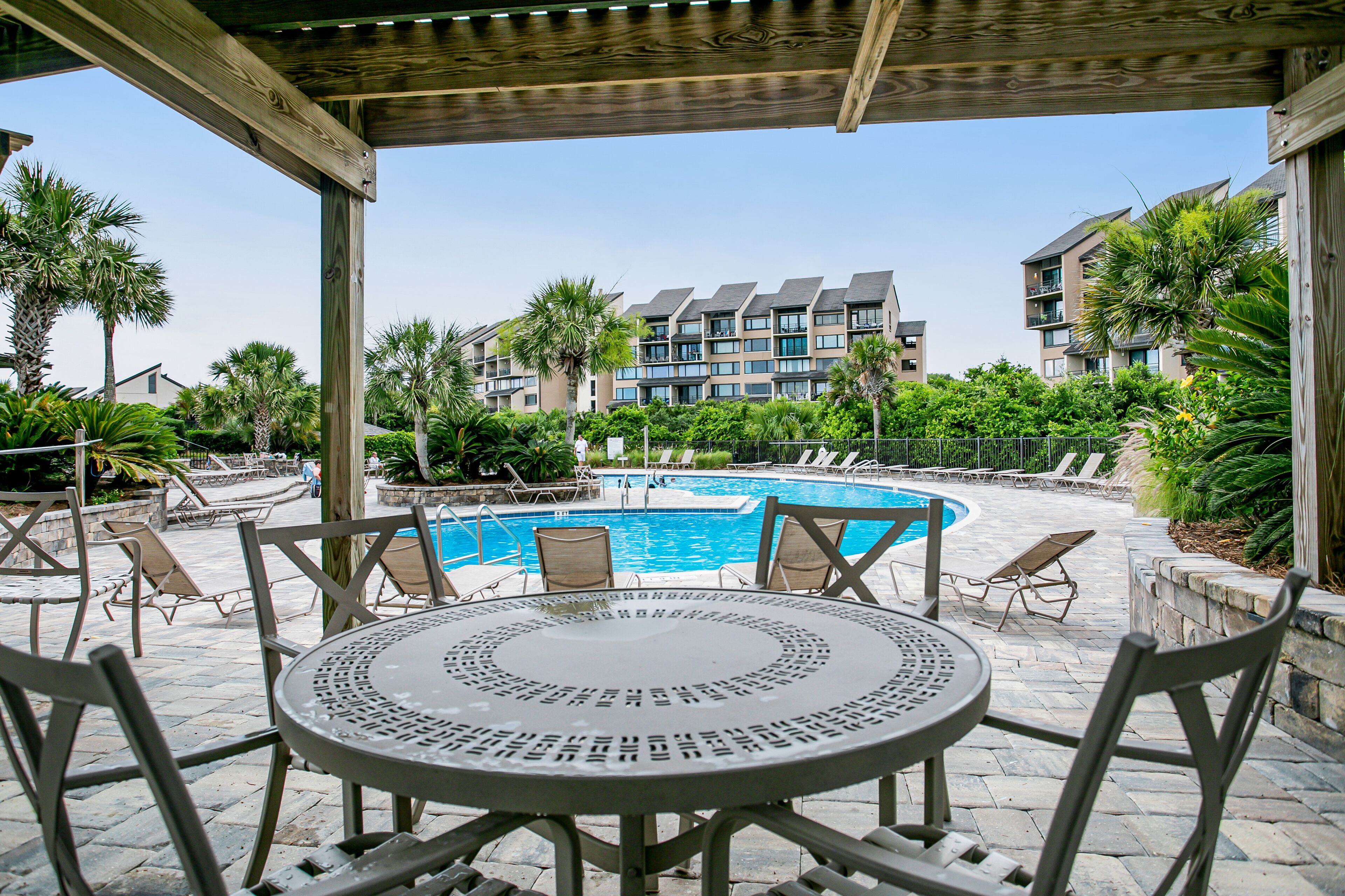 A poolside area with a round table and chairs, a pool, and a view of multi-story buildings in the background.