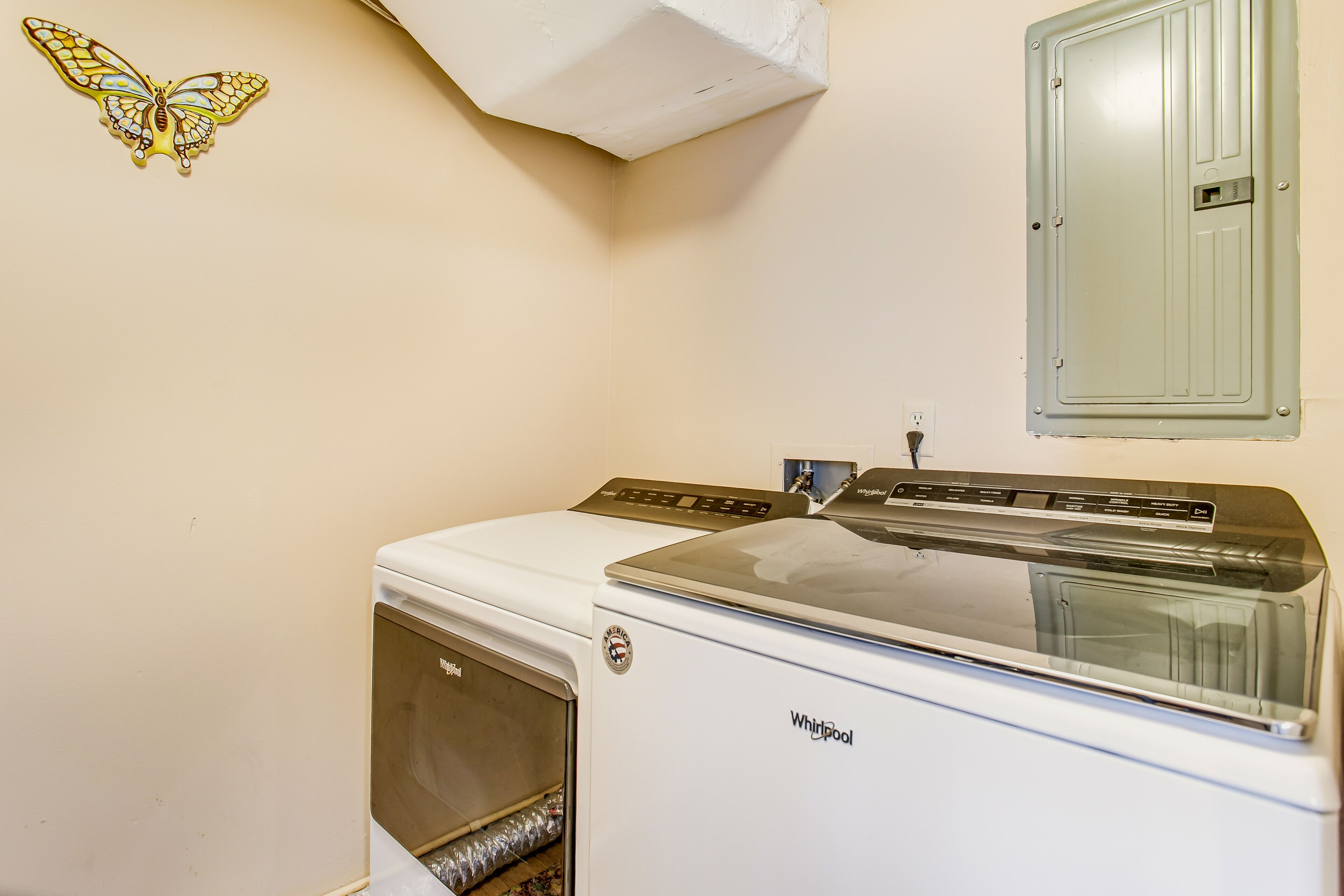 A compact, white Whirlpool washer and dryer unit in a laundry room with a wall-mounted butterfly decoration.