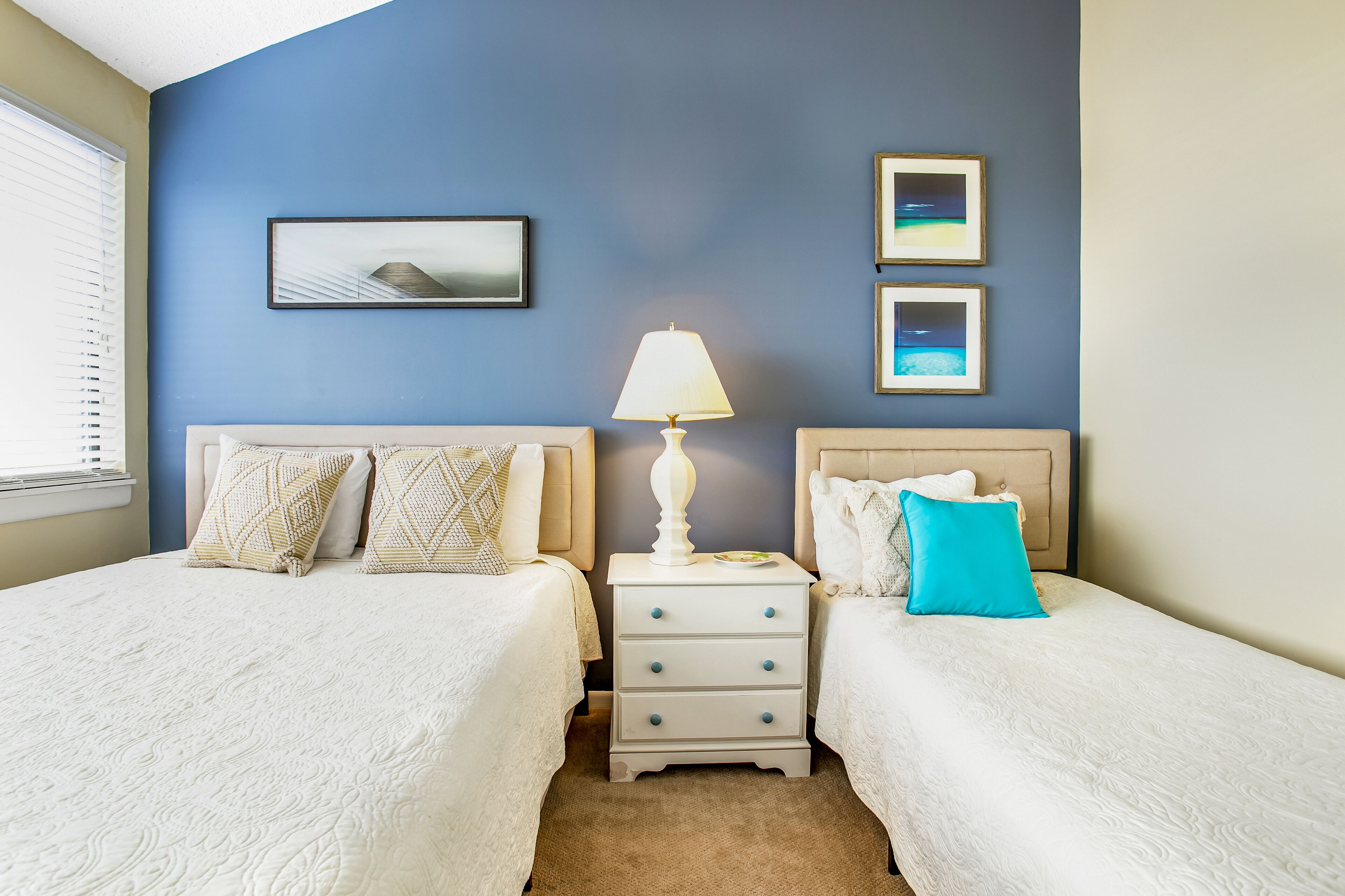 A bedroom with two beds, a nightstand with a lamp, and framed pictures on the wall.