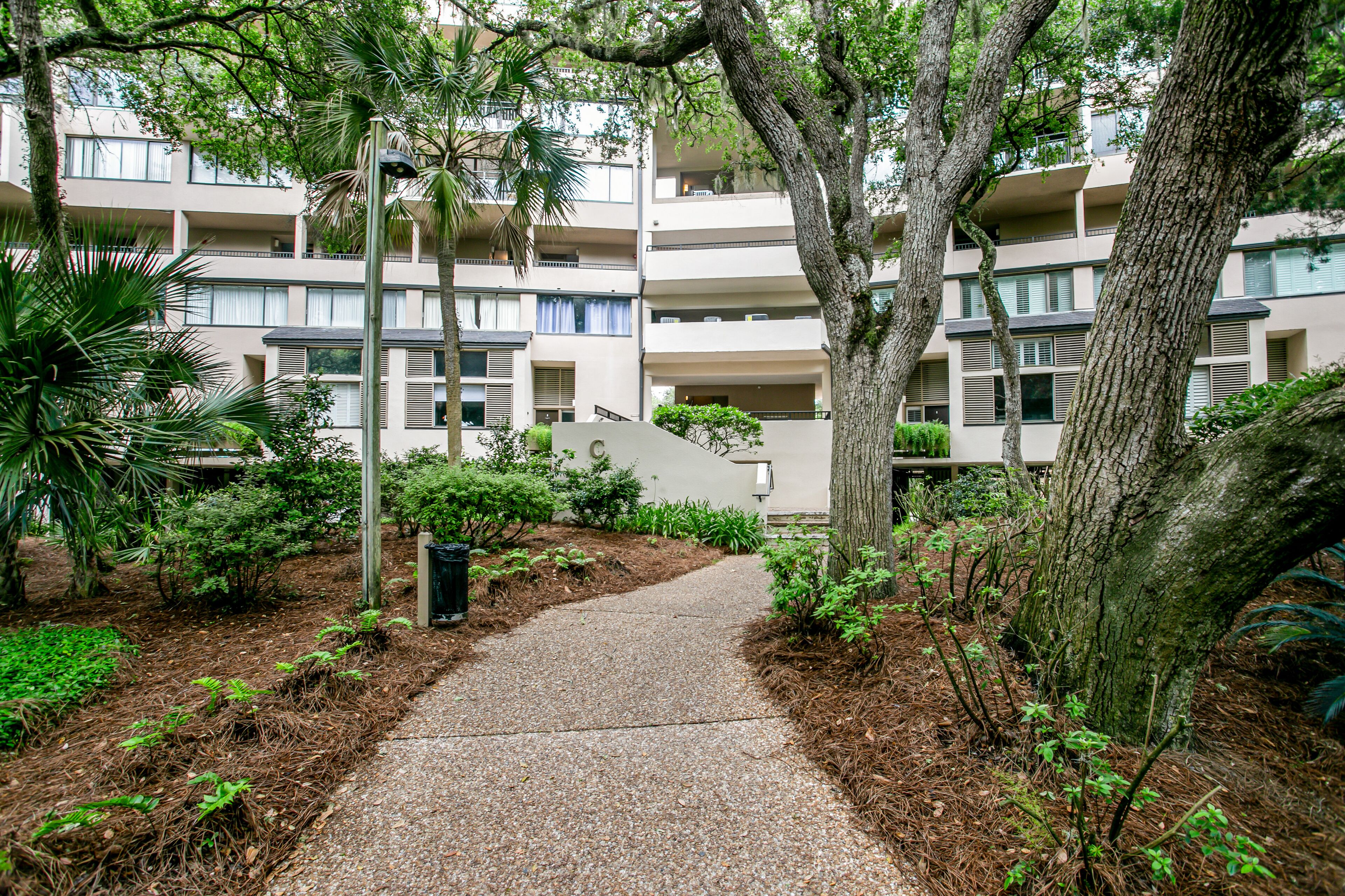 A pathway leading to a multi-story building surrounded by trees and shrubs.