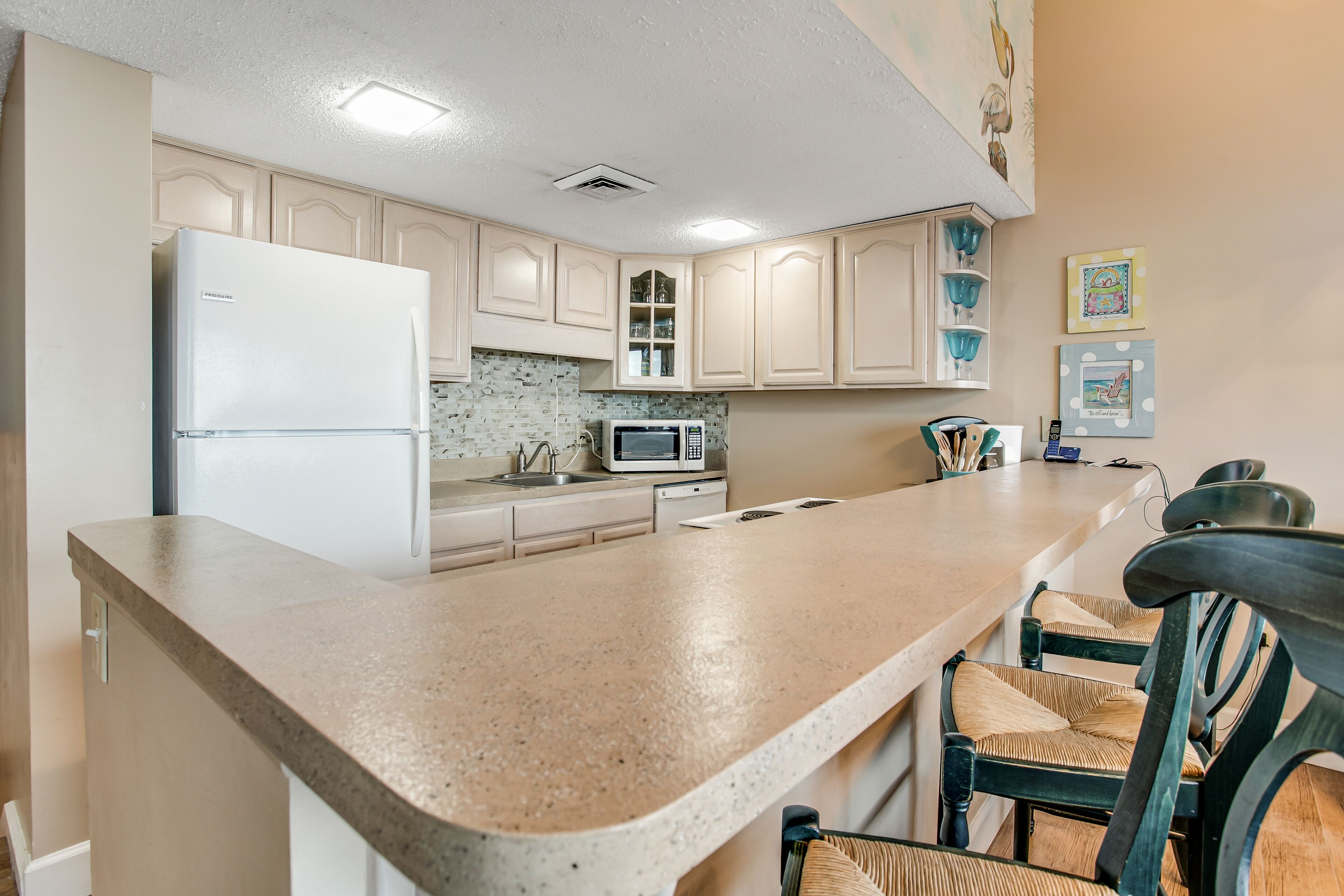 A kitchen with a refrigerator, microwave, and a sink. There are chairs and a countertop.