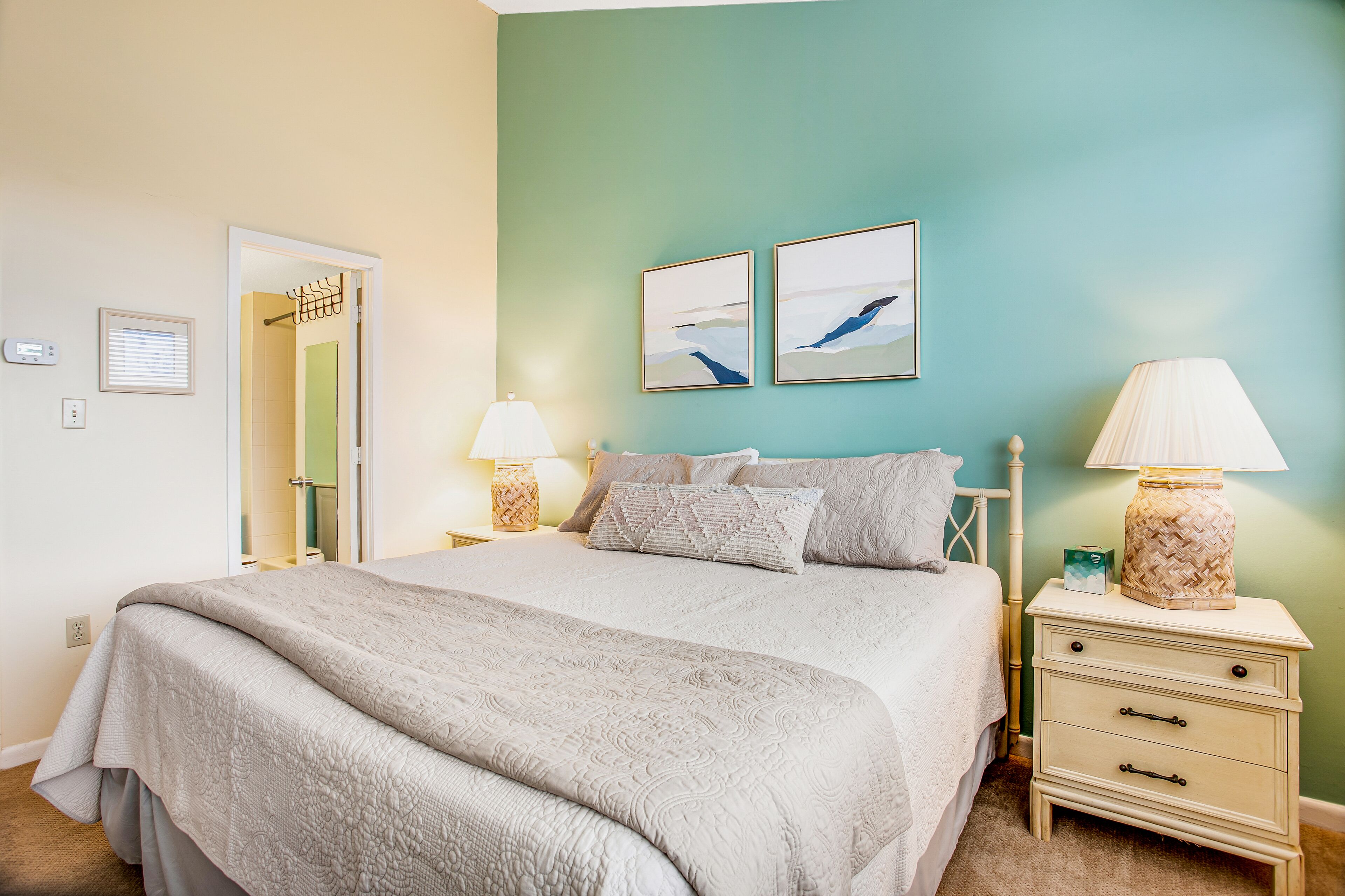 Een slaapkamer met een bed, twee nachtkastjes, een lamp en twee aan de muur bevestigde afbeeldingen.