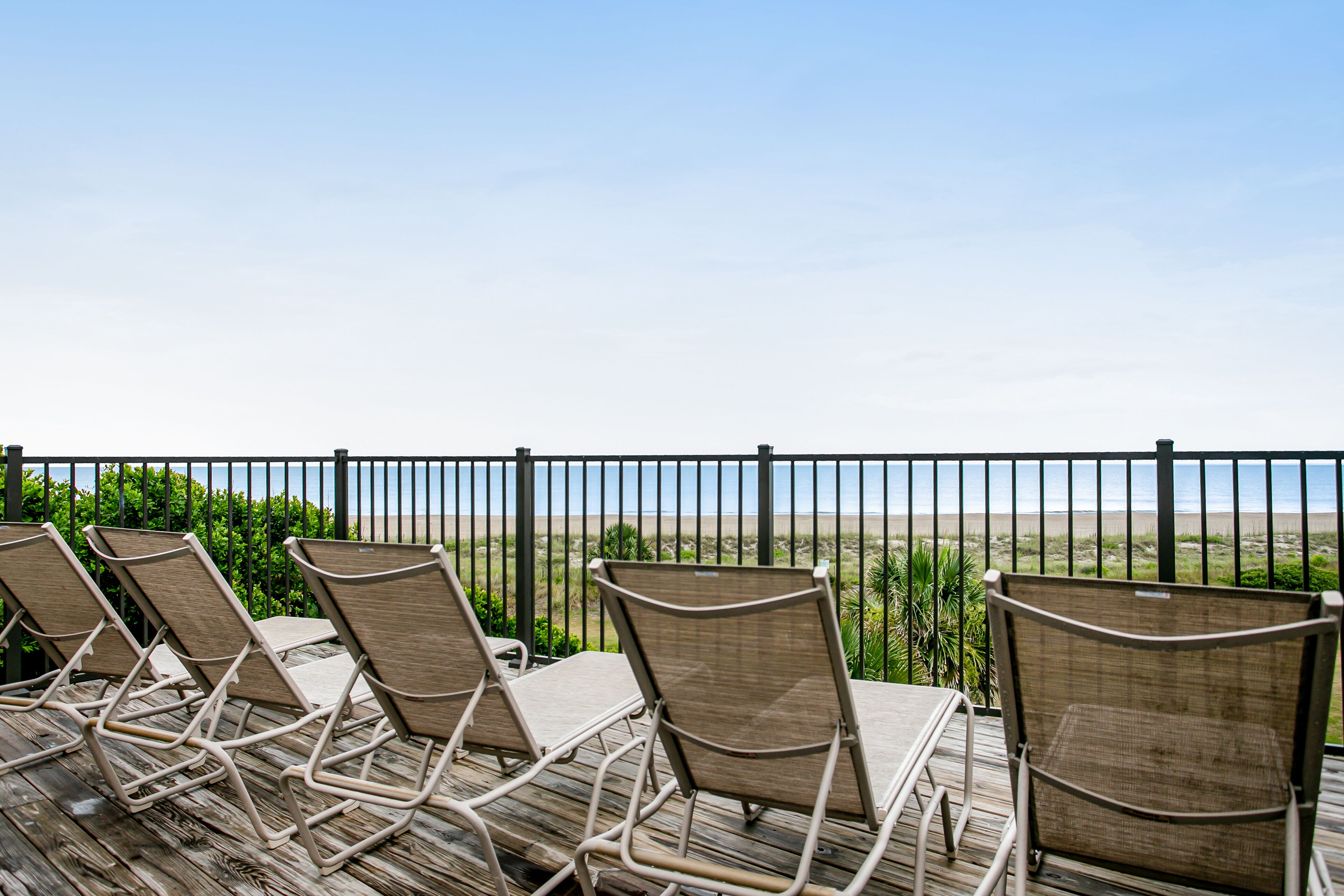 A deck with lounge chairs facing a beach view, enclosed by a metal railing.