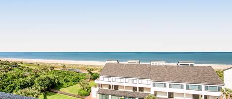 A two-story building with a flat roof, large windows, and a view of the beach.