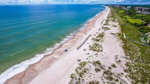Luchtbeeld van een strand met een rij strandparasols en een complex van gebouwen op de achtergrond.
