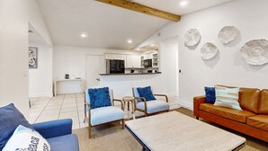Un salon moderne avec un canapé, deux fauteuils, une table basse et une cuisine en arrière-plan.