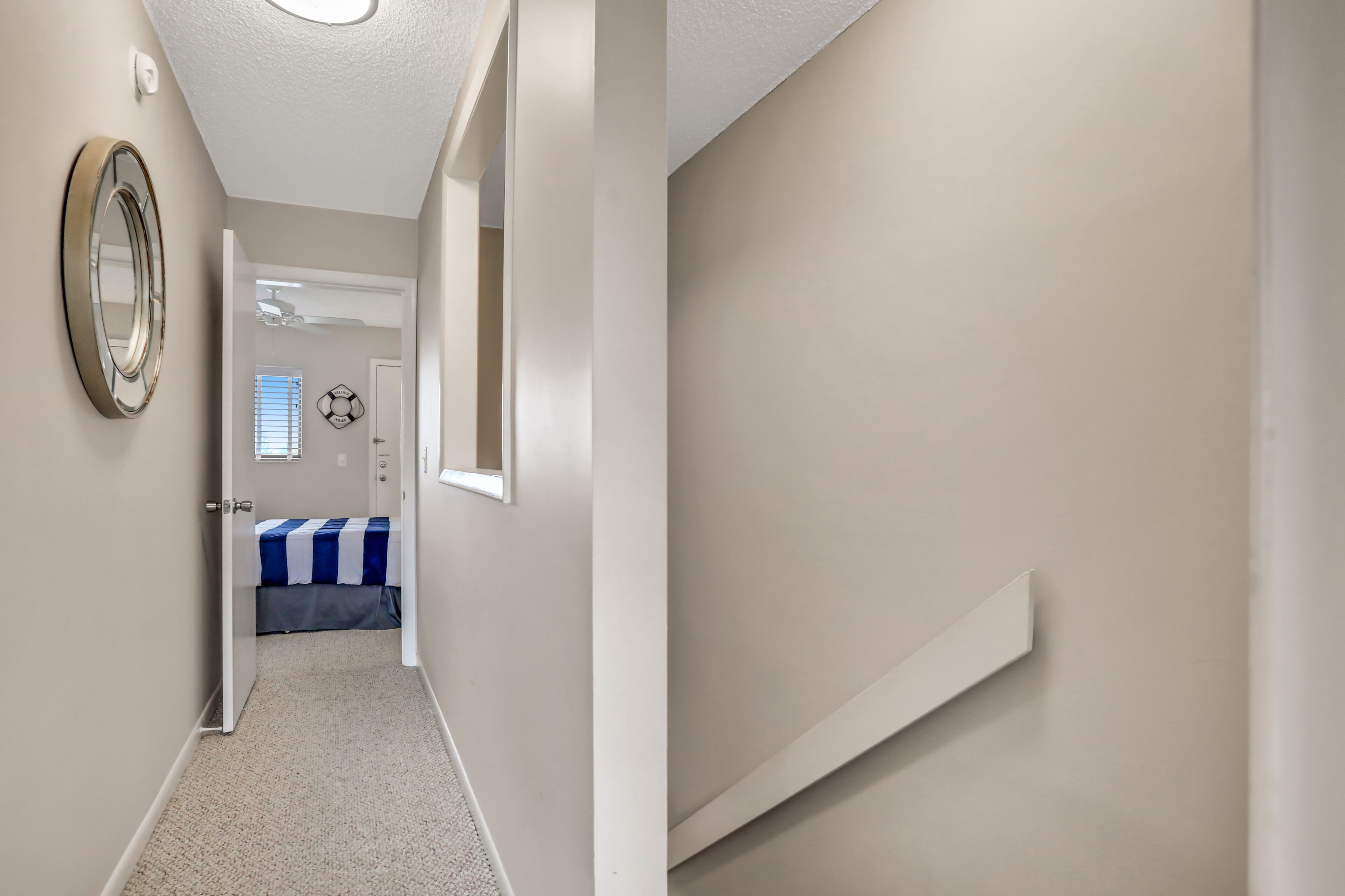 Un couloir avec un lit, un miroir et une porte donnant sur une autre pièce.