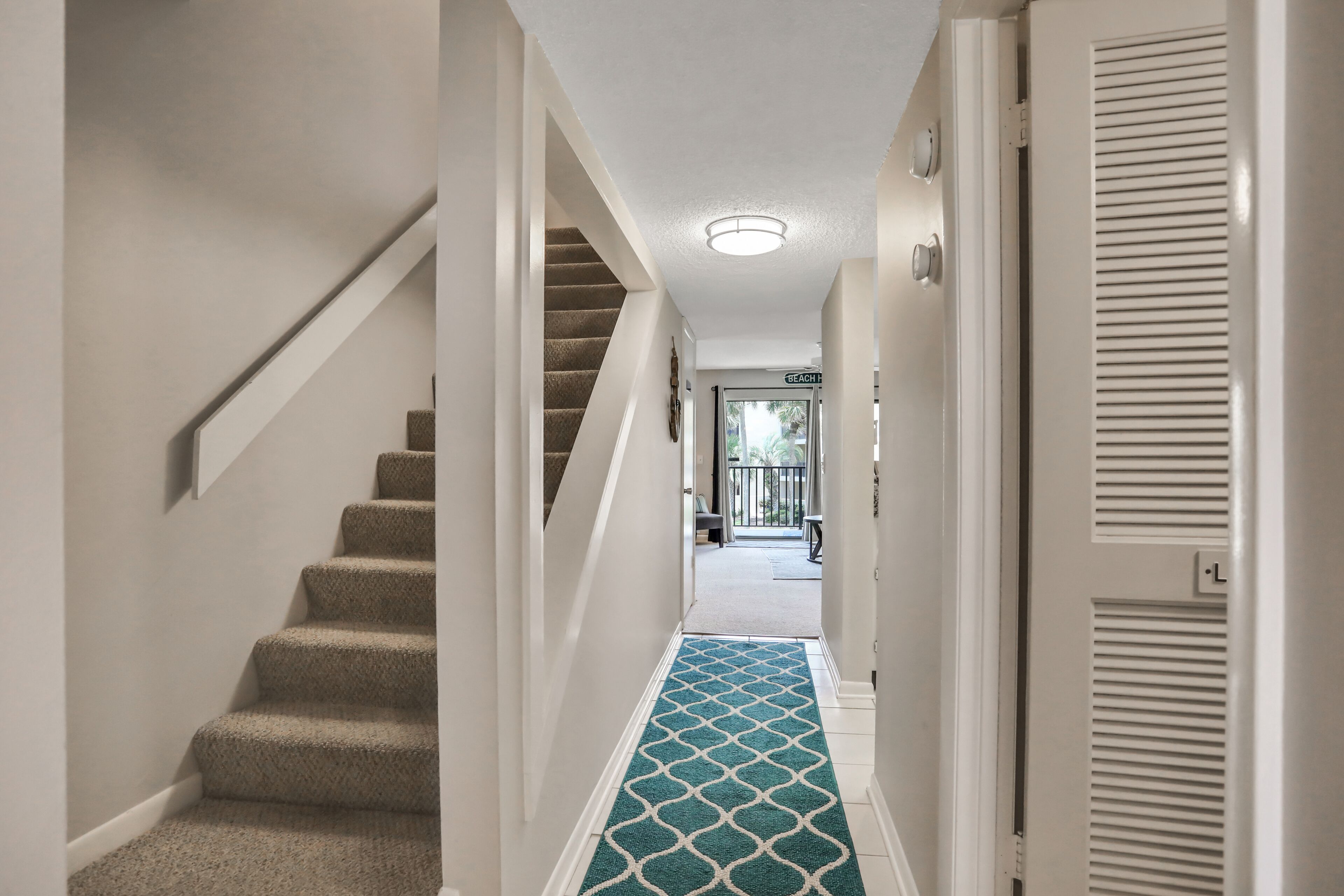 Un couloir avec un escalier recouvert de moquette menant à une porte sur laquelle est inscrit « MAISON DE PLAGE ».