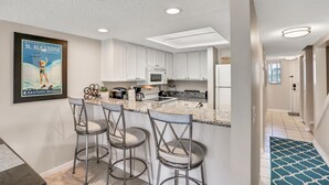 Eine moderne Küche mit weißen Schränken, einer Granitabdeckung und einer Bar mit Metallstühlen.