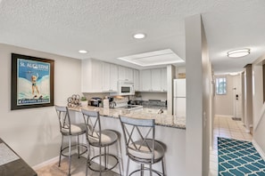 A modern kitchen with white cabinets, a granite countertop, and a bar area with metal chairs. - Ocean-view Condo With 2 Pools, Beach Access & Private Lanais (St. Augustine)