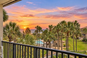 A balcony with a view of a sunset over the ocean, palm trees, and a swimming pool. - Ocean-view Condo With 2 Pools, Beach Access & Private Lanais (St. Augustine)